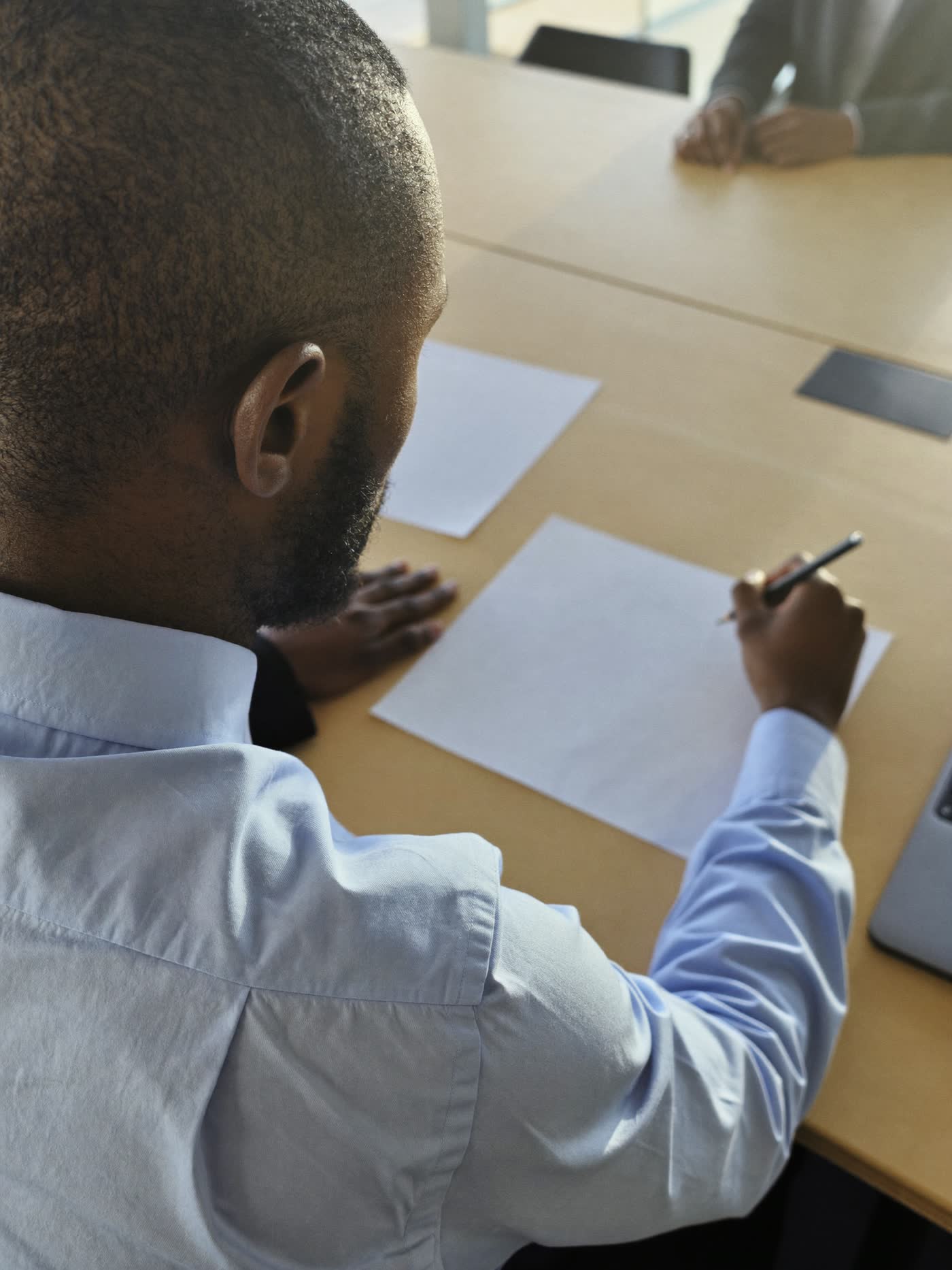 A professional sketching on paper beside a laptop while a facilitator leans in to look